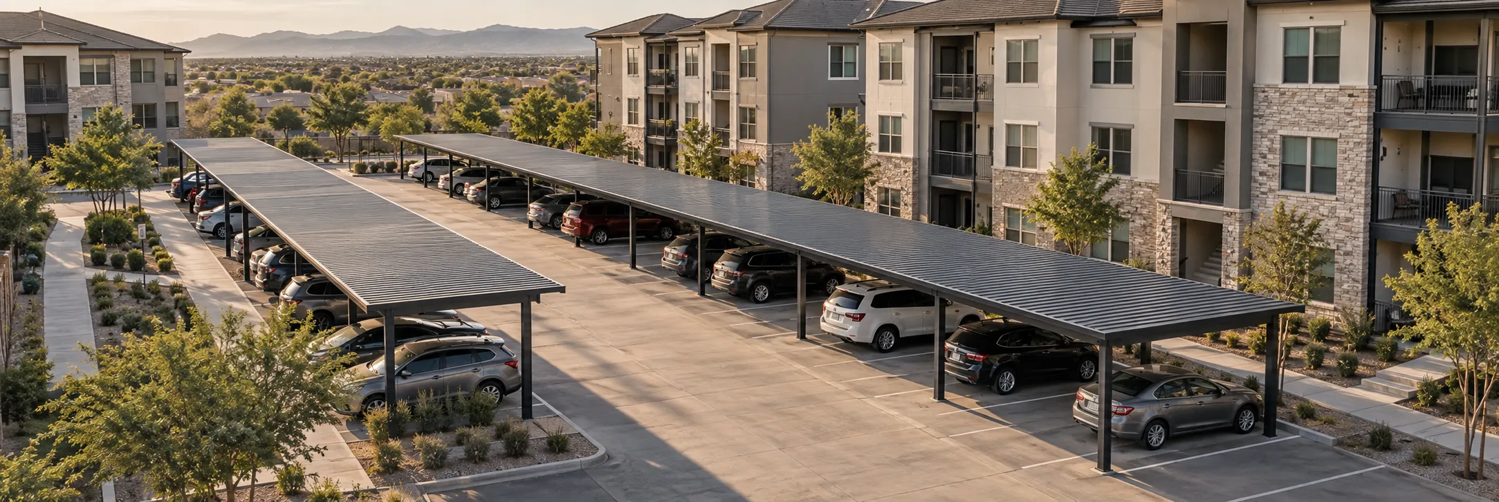 Elevated view of steel carports covering resident parking beside a multifamily apartment building, with clear drive aisles and walkways.